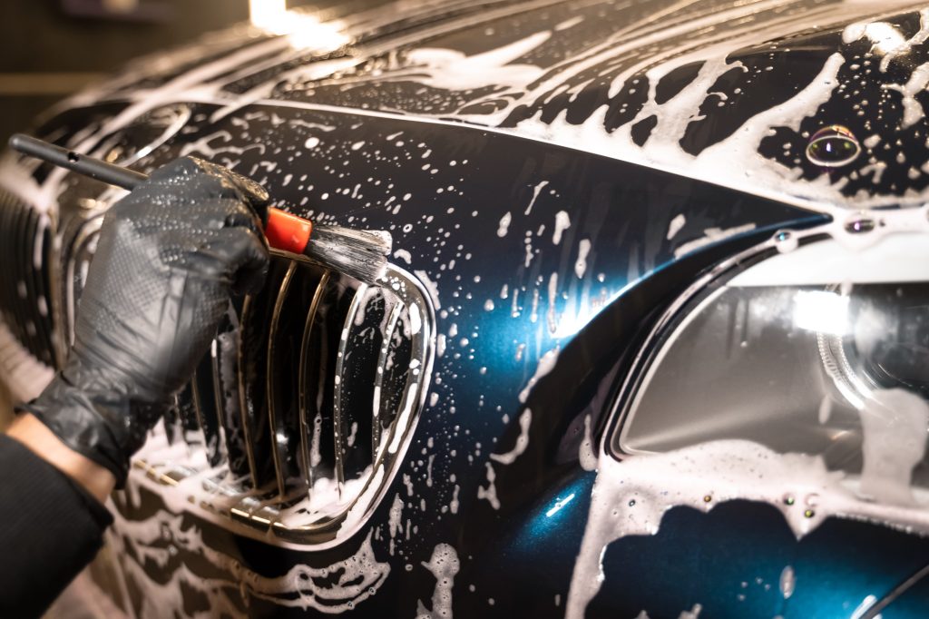 Detailed car wash. Detailing center worker cleans car's radiator grill with brush Detailed car wash. Detailing center worker cleans car's radiator grill with brush
